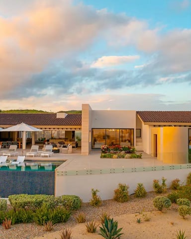 Modern beige villa with pool, lounge chairs, and desert landscaping at sunset