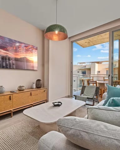 Modern living room with gray sofa, wooden sideboard, pendant light, and glass doors opening to a balcony with city views