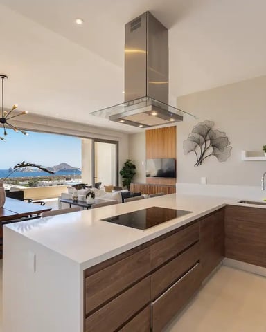Modern kitchen with island, stainless steel range hood, and ocean view through floor-to-ceiling windows