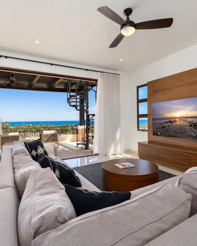 Modern living room with ocean view, gray sectional sofa, wood TV wall, and open patio overlooking blue sea