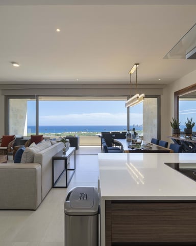 Open-plan living room and kitchen with ocean view, modern furnishings, and floor-to-ceiling windows overlooking coastline