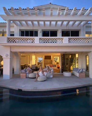 White modern villa with pergola, pool terrace, and lounge seating overlooking illuminated interior at dusk