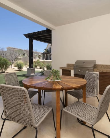 Covered patio with round wooden dining table, woven chairs, built-in grill, and desert landscape view