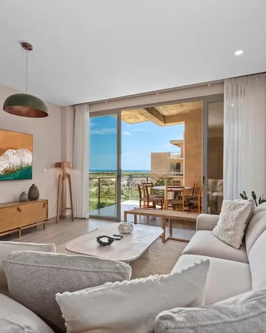 Modern living room with gray sofa, wooden furniture, wall-mounted TV, and ocean view through glass doors