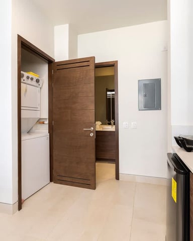 Modern kitchen with wood cabinetry, white countertops, stainless steel appliances, and open doorway to laundry area