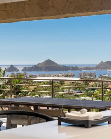 Covered terrace with dining table overlooking coastal bay, mountains, and beachfront buildings