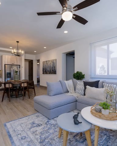 Open-plan living room and kitchen with gray sectional sofa, white coffee tables, dining area, and stainless steel appliances.