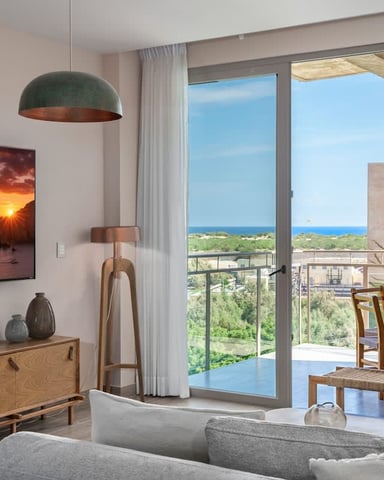 Modern living room with ocean view through floor-to-ceiling windows, mid-century furniture, and coastal landscape artwork.