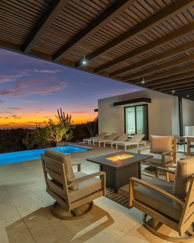 Modern patio with infinity pool, fire pit seating, pergola, and sunset ocean view at dusk