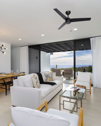 Modern open-plan living and dining area with ocean view, white sofa, wooden dining table, and glass doors opening to terrace