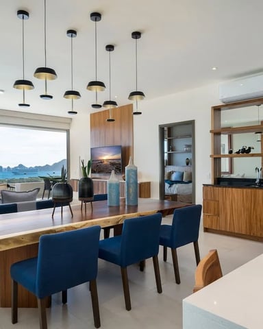 Modern open-plan living space with dining table, ocean view through floor-to-ceiling windows, and pendant lighting overhead