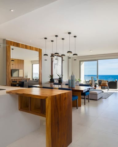 Modern open-plan kitchen and living room with ocean view, wood island, stainless steel appliances, and pendant lighting.
