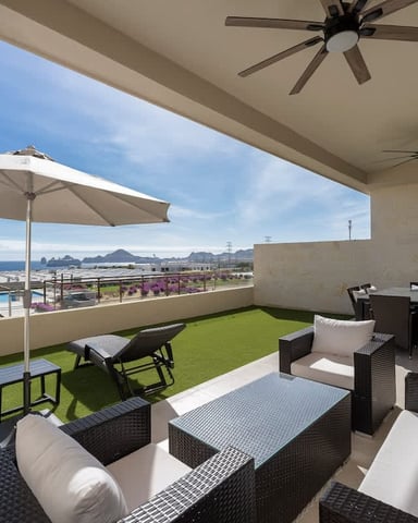 Rooftop terrace with lounge seating, artificial turf, umbrella, and ocean view with mountains in distance