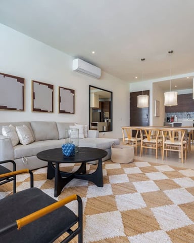 Open-plan living room with gray sofa, black chairs, black coffee table, and kitchen with wooden bar seating in background