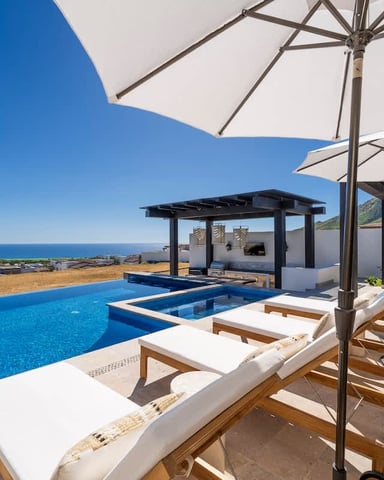 Luxury villa terrace with infinity pool, white umbrellas, lounge chairs, and Mediterranean Sea view