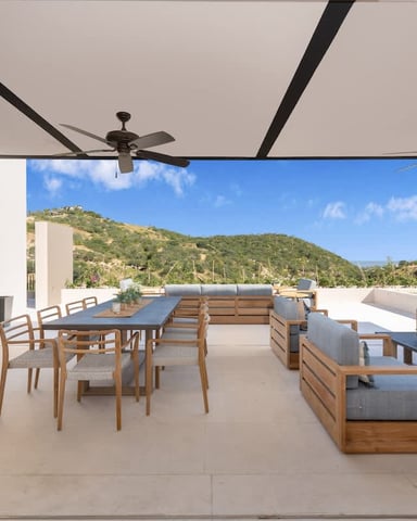 Rooftop terrace with dining table, wooden lounge seating, ceiling fans, and hillside views