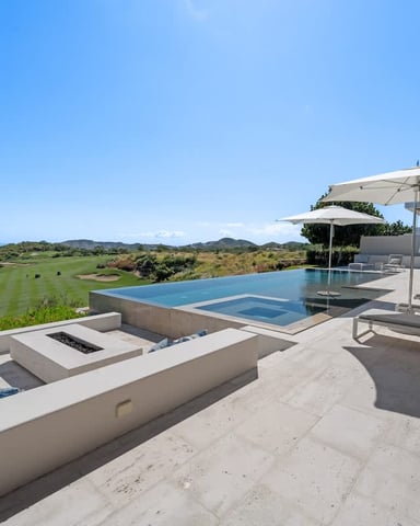 Modern terrace with infinity pool, loungers, umbrellas, and golf course views overlooking Mediterranean coastline