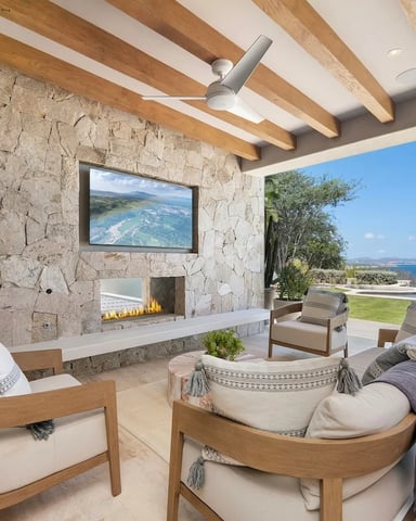 Modern living room with stone fireplace, wooden beam ceiling, and ocean view through open glass doors to terrace