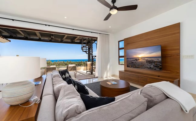 Modern living room with ocean view, gray sectional sofa, wood media wall with TV, and open patio overlooking blue sea