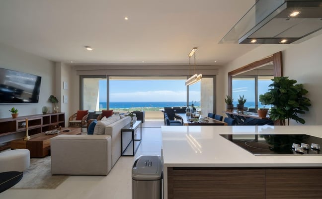 Modern open-plan living room and kitchen with ocean and coastline views through floor-to-ceiling windows